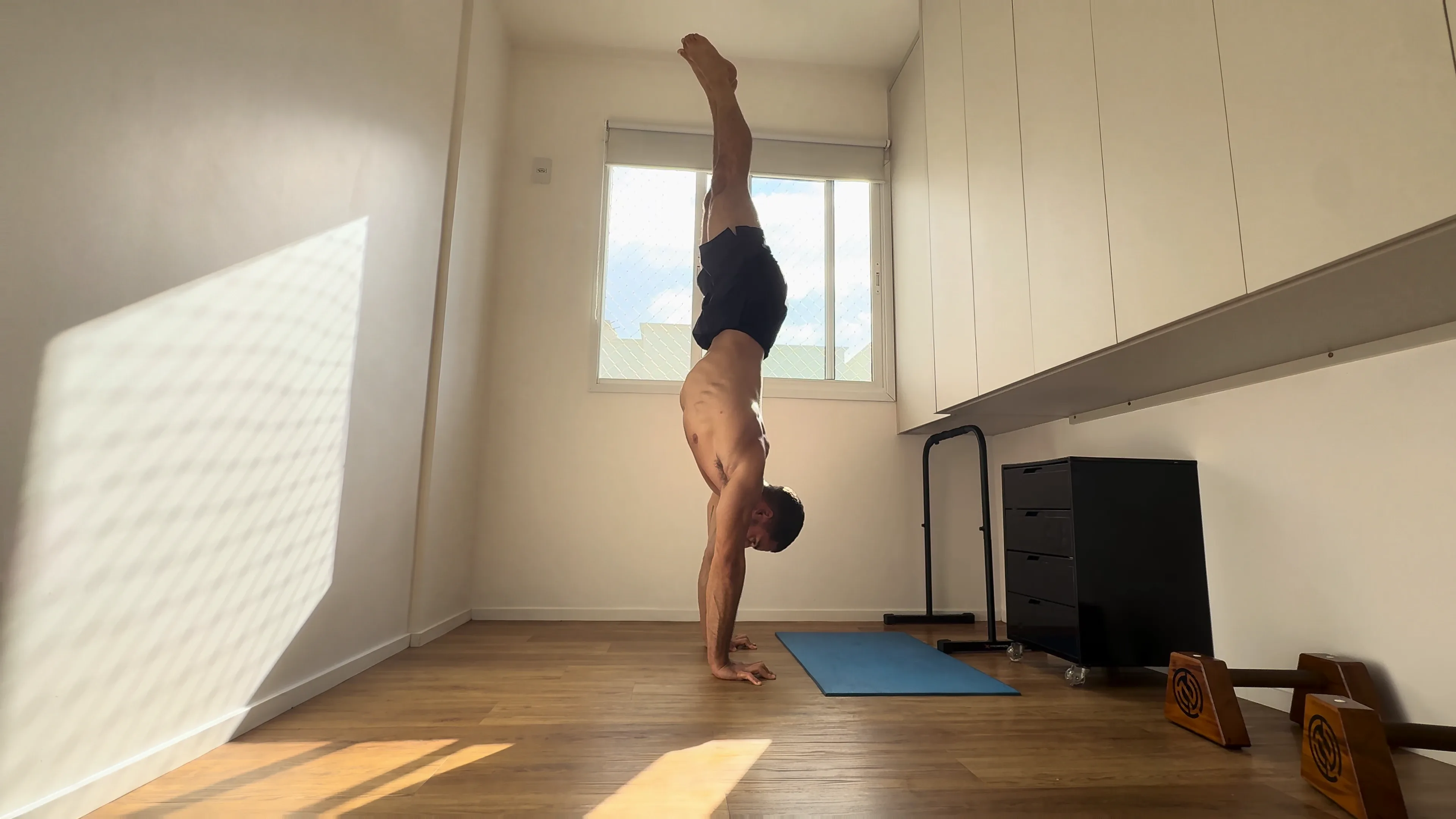 O Luca numa parada de mão livre na sala, com o sol da manhã entrando pela janela.