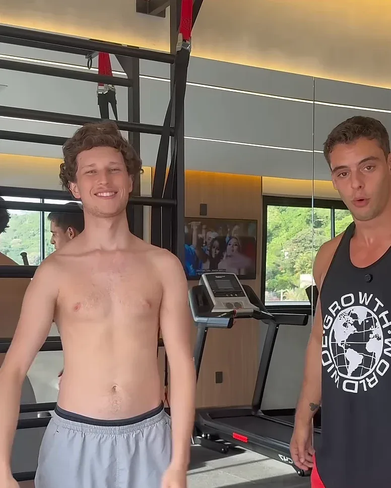 O Diogo, à esquerda, sorrindo, sem camisa, ao lado do Luca de regata preta, numa academia