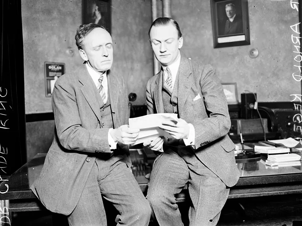 Foto de 1929, em preto e branco: o Dr. Arnold Kegel, à direita, de terno, sentado na beira de uma mesa com o Dr. Clyde King, os dois lendo uma folha de papel, num escritório em Chicago