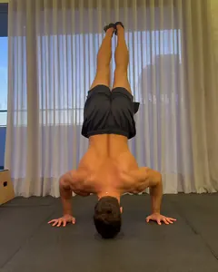 O Luca em parada de mão livre, no meio da sala, no fundo da flexão, com a cabeça perto do chão.